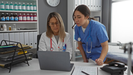 Women doctors and nurse in clinic room reviewing patient data on laptop indoors indicating collaboration in healthcare workplace environment