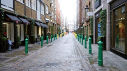 Fototapeta premium Blurred view of a cobblestone street in london with bokeh effects, showcasing green poles and classic architecture during winter or autumn.
