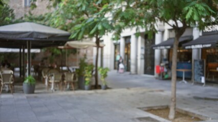 Defocused street scene in barcelona with blurred outdoor cafe seating and lush greenery under a mild bokeh effect enhancing the urban atmosphere of the european city.