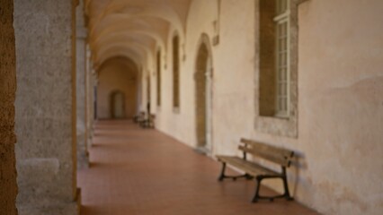 Blurred image of an old university campus corridor with benches and archways, showcasing a serene and historic outdoor setting with bokeh effect.