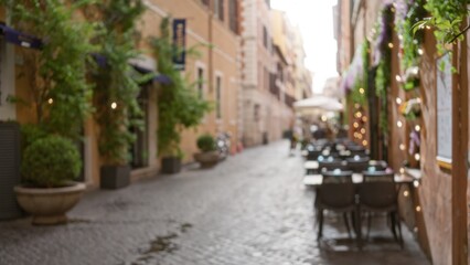 Fototapeta na wymiar Blurred street scene in old town rome with bokeh effect showing charming italian outdoor cafe and cobblestone walkway lined with flowering plants and colorful buildings.
