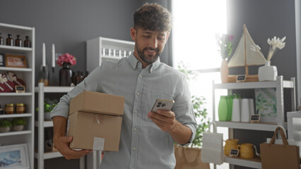 Young man holding packages and looking at his phone in a well-decorated home decor store,...
