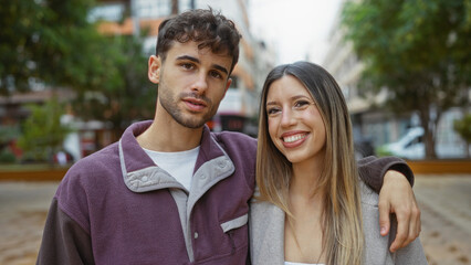 Couple smiling together in an urban street with a man and woman standing closely, showcasing happiness and love in an outdoor city environment.