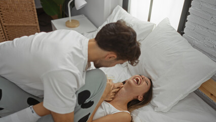 Man giving woman tickles as they laugh together on the bed, showcasing intimate couple moments in a...
