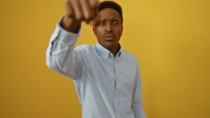 Young african man posing against a yellow background with a focused expression wearing a blue shirt...