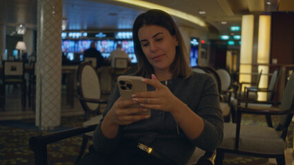 Woman relaxing in luxury bar using smartphone, capturing modern lifestyle, hispanic young woman indoors, chic ambiance visible around her, elegantly enjoying evening.
