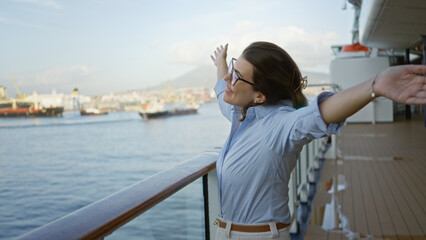 Fototapeta premium Woman enjoying cruise outdoors on a sunny day at dock with arms outstretched showcasing freedom and happiness with beautiful ocean view in background.
