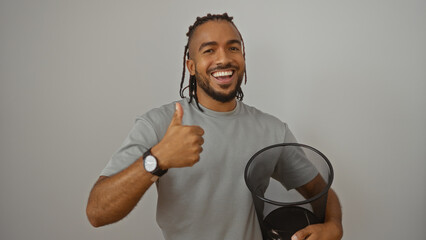 Young man with braids and a watch giving a thumbs-up while holding a basket, smiling confidently...