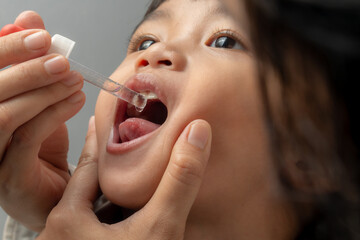 A mother gives her young child vitamins using a dropper