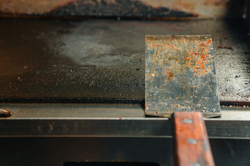 A dirty stainless steel spatula resting on a flat griddle, dirty kitchen concept