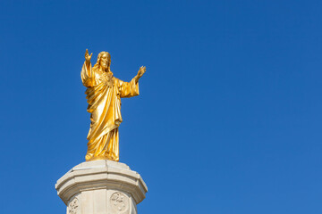 Obraz premium Golden Jesus Christ statue on a pillar with a clear blue sky. At the Basilica of Our Lady of the Rosary, Sanctuary of Fatima, Portugal.