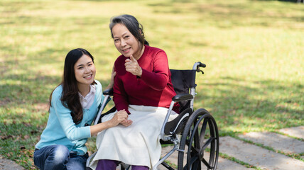 Fototapeta premium Asian senior woman in wheelchair with happy daughter. Family relationship retired woman sitting on wheelchair in the park age care at retirement home.