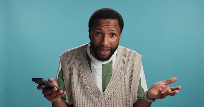 Confused, black man or phone with bad news for fraud, online scam or rejection on a blue studio background. Portrait, male person or African model with mobile smartphone for disapproval or broken app