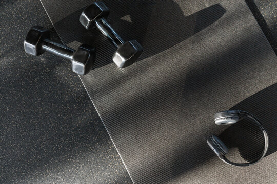 Black dumbbells for sports and acoustic headphones lie on the floor in the gym on a stylish yoga mat