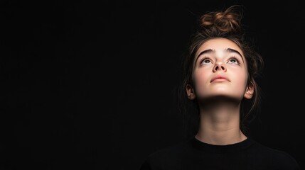 a girl with a black top looking up at you Over black Studio Background.
