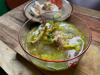 typical Indonesian food, chicken soto complete with claw and koya toppings, very suitable to be eaten with rice, boiled eggs, lime juice served in a glass bowl on a wooden table background