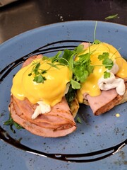 Eggs Benedict. The meal is served on a square, white plate against a dark background, providing a lovely contrast that makes the dish the focal point.
Two halves of an English muffin form the base of 