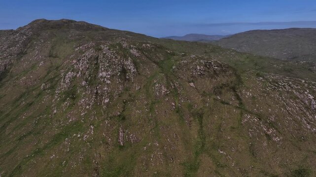 Barnesmore Gap, County Donegal, Ireland, June 2023. Drone slowly orbits counte rclockwise and pulls back showcasing the exposed grey rmountain peak revealing the meandering N15 road in the distance.