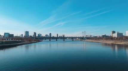 Naklejka premium Cityscape Panorama: River, Bridge, and Skyline under a Clear Blue Sky