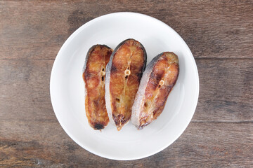 Sun-dried pangasius in a white ceramic plate on a wooden table.