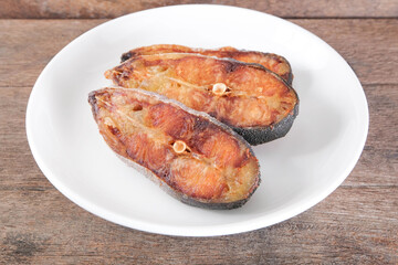 Sun-dried pangasius in a white ceramic plate on a wooden table.
