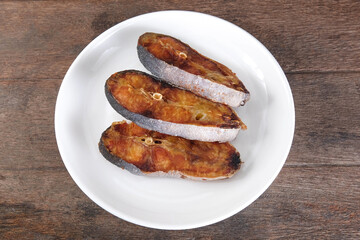 Sun-dried pangasius in a white ceramic plate on a wooden table.