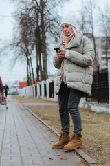 Fototapeta premium A beautiful young woman strolls through the city on a sunny autumn day, happily chatting on her phone. She smiles and laughs, radiating joy and positive energy in the vibrant urban setting