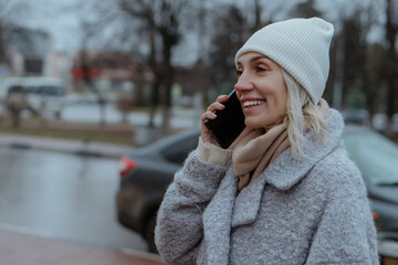 Smiling young woman walking through a frosty city street on a winter morning, talking on her...