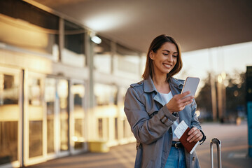 Happy female traveler using smart phone at airport.