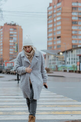 Smiling young woman walking through a frosty city street on a winter morning, talking on her...