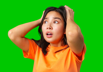 Young woman shows surprise and shock while holding her head with hands in front of bright green...
