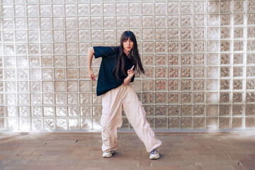 Young dancer performs expressive moves against glass block wall in urban environment during daytime