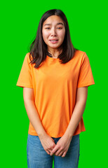 Young woman in orange shirt smiles nervously against a bright green background in a casual setting