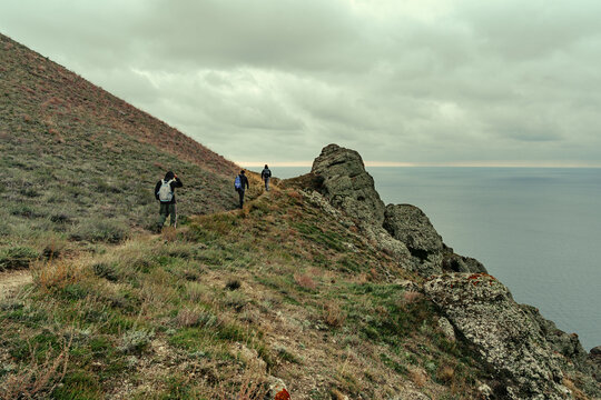 Hikers explore a rugged coastal path during a cloudy day by the ocean in a remote location