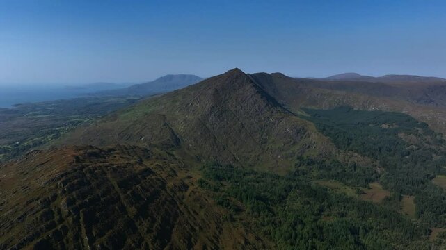 Sugarloaf, Caha Mountains, County Cork, Ireland, September 2024. Drone slowly pushes forwards with a view of rugged peaks, dense forests, and serene landscapes with the Atlantic ocean in the distance.