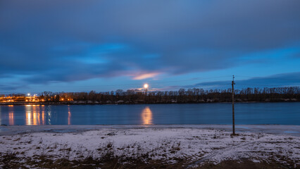 Fototapeta premium Night landscape with moon in the sky, river, silhouettes of trees, lights of town.