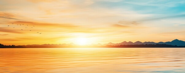 Obraz premium A serene sunset over calm waters, with vibrant orange and blue hues reflecting across the sky and the landscape of distant mountains.