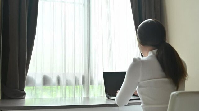 Rear view of Asian woman while typing on her laptop in bedroom. Footage of woman doing work at home.