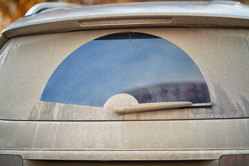Dirty car rear window obstructed by salt stains and dry mud from winter roads, need for proper...