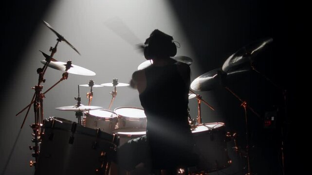 Skilled drummer punching hi-hats, playing music in rock gig, rearview in dark. Hobby and passion, young adult man rehearsing to beat rhythm, enjoy modern music, cool guy rocking crowd in concert hall