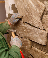 A man is working on a wall, using a hammer and chisel to shape a stone