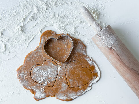 Heart shaped cookie cutouts on floured dough with rolling pin