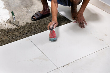 Skilled worker repairing and tiling floor in house or office. Construction worker installing tiles and self-leveling for building and renovation interior walkway.