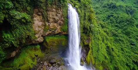 Fototapeta premium Majestic waterfall cascading down rocky cliff surrounded by lush greenery