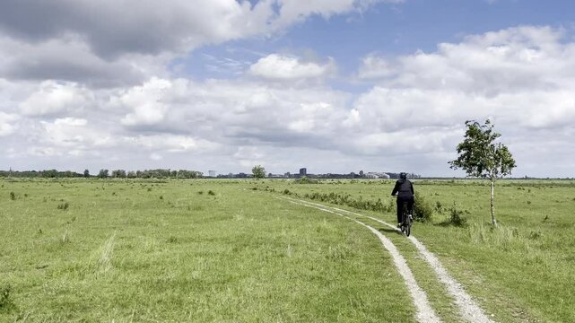 Woman cycling on gravel road through Amager Naturpark with Copenhagen skyline in the background