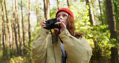 A young woman takes pictures of nature with a camera while standing in the forest. Close-up of her face