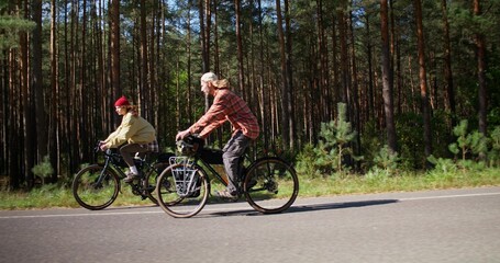 Fototapeta premium A young man and a woman ride bicycles along the road along the forest, side view