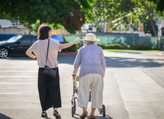 Senior woman walking using a mobility walker in the carpark. Adult daughter adjusting elderly...