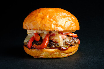 Savoring a Gourmet Burger With Grilled Peppers and Melted Cheese in a Crisp Golden Bun, Served Against a Sleek Black Background