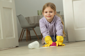 Cute little girl wearing protective rubber gloves while cleaning the floor with wet cloth.	
